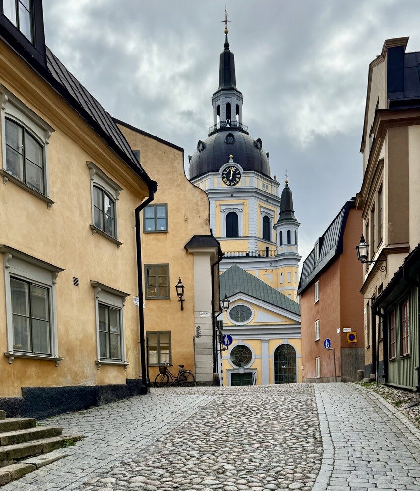 A narrow cobbled street in a Swedish old town leading up to a church tower, lined with traditional ochre and pale buildings.
