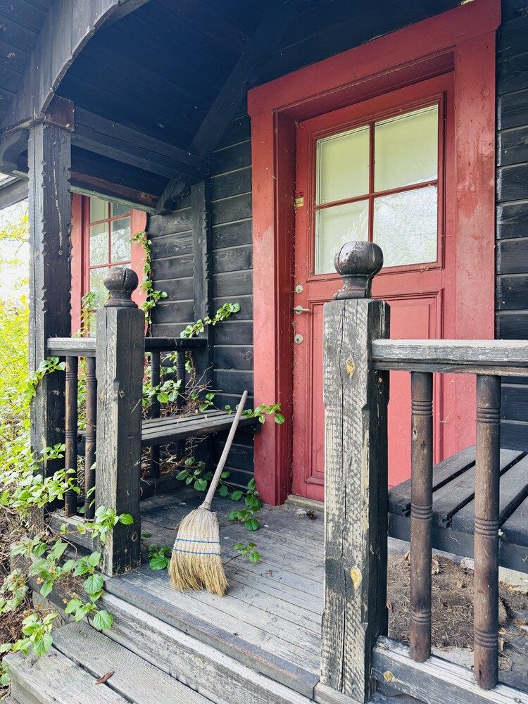 The corner of a red-painted Swedish timber cabin with a bright red door and white-framed windows.